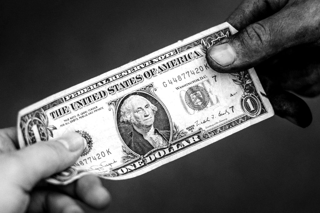 A hand holding out a US one-dollar bill